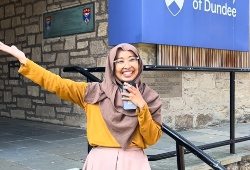 student standing on steps leading to a building with University of Dundee sign